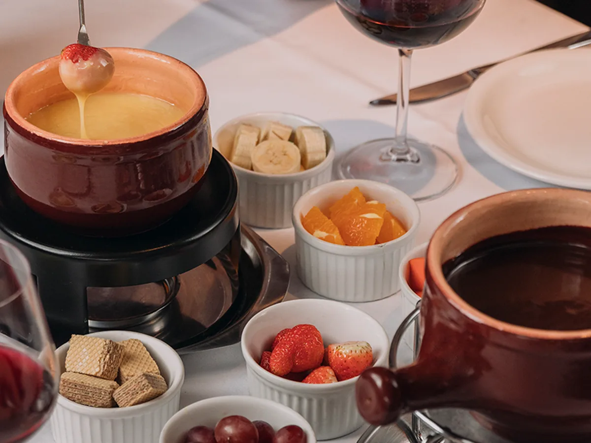 Mesa com fondue de chocolate, frutas, wafer e taças de vinho